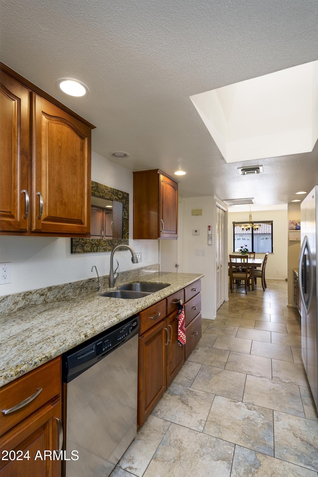 kitchen featuring pendant lighting, sink, a textured ceiling, appliances with stainless steel finishes, and light stone counters