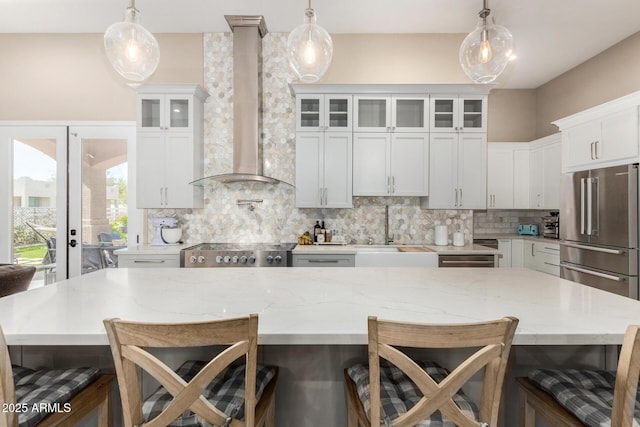 kitchen featuring a breakfast bar area, tasteful backsplash, a sink, high end fridge, and wall chimney exhaust hood
