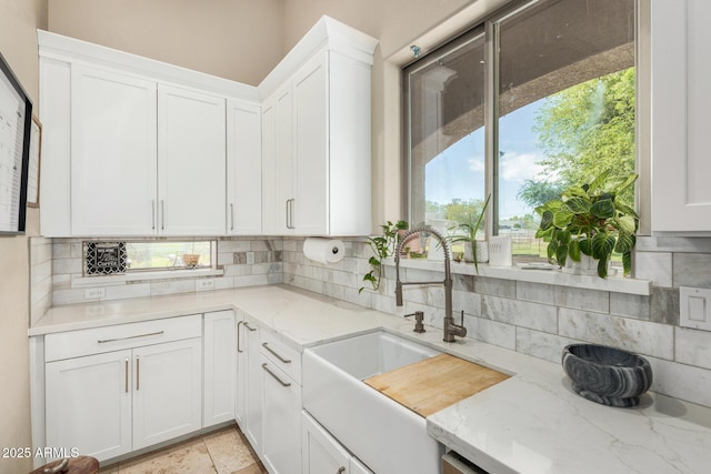kitchen with a sink, light stone counters, tasteful backsplash, and white cabinets