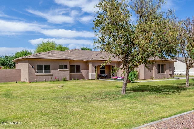 back of property featuring a lawn, fence, a tile roof, and stucco siding