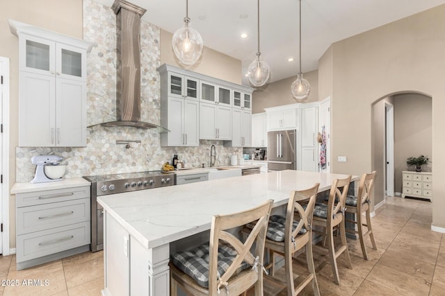 kitchen featuring wall chimney range hood, a sink, a center island, stainless steel appliances, and tasteful backsplash