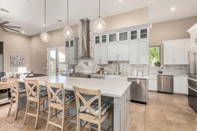 kitchen with stainless steel dishwasher, a sink, decorative backsplash, and wall chimney range hood