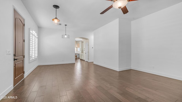 interior space with baseboards, a ceiling fan, arched walkways, and wood finished floors
