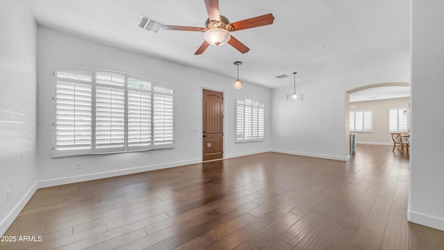 unfurnished living room featuring arched walkways, a ceiling fan, baseboards, wood finished floors, and visible vents