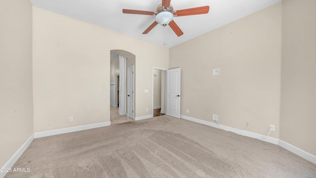 empty room featuring arched walkways, a ceiling fan, baseboards, and carpet
