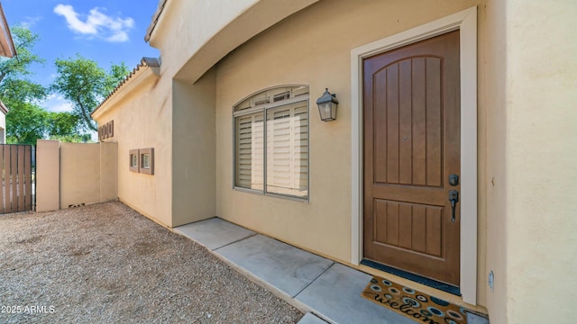 view of exterior entry with a gate, stucco siding, and fence