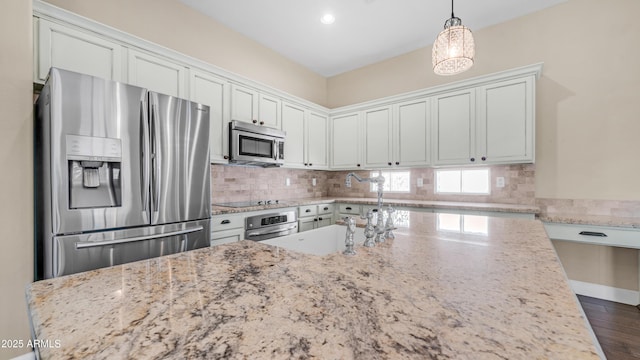 kitchen with hanging light fixtures, appliances with stainless steel finishes, decorative backsplash, and light stone counters