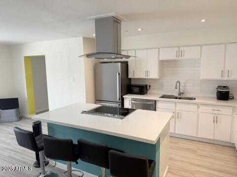 kitchen featuring white cabinets, stainless steel appliances, island exhaust hood, and a sink
