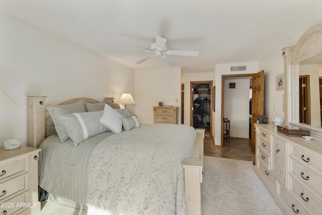 bedroom featuring a walk in closet, light carpet, a textured ceiling, a closet, and ceiling fan