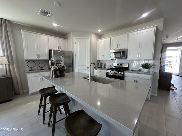 kitchen featuring visible vents, white cabinets, an island with sink, stainless steel appliances, and a sink