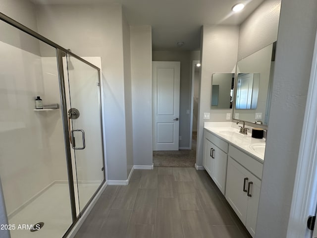 full bathroom featuring baseboards, double vanity, a sink, and a shower stall