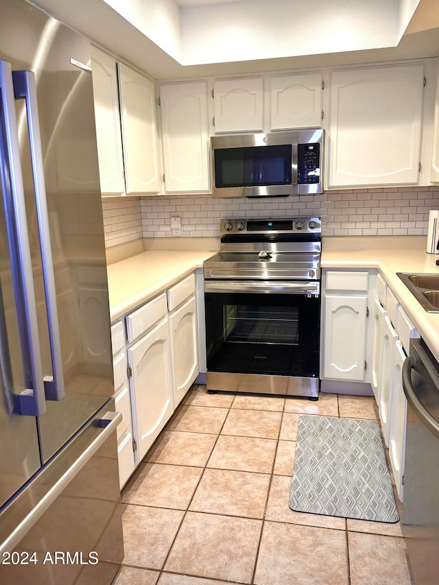 kitchen featuring tasteful backsplash, white cabinetry, light tile patterned floors, and stainless steel appliances