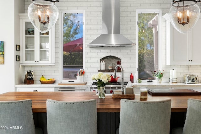 kitchen featuring white cabinets, wall chimney exhaust hood, a wealth of natural light, and hanging light fixtures