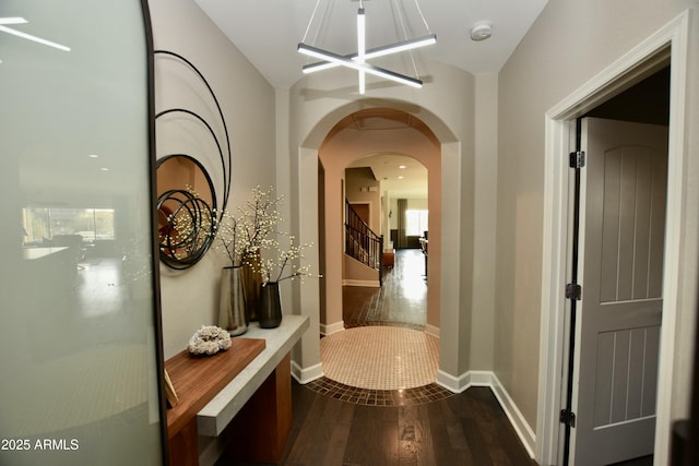 hallway with dark wood-type flooring, arched walkways, stairway, and baseboards