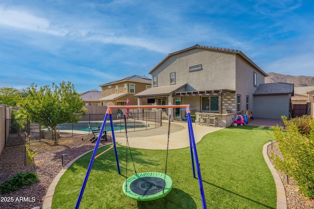 view of play area with a yard, exterior bar, a fenced in pool, and a patio
