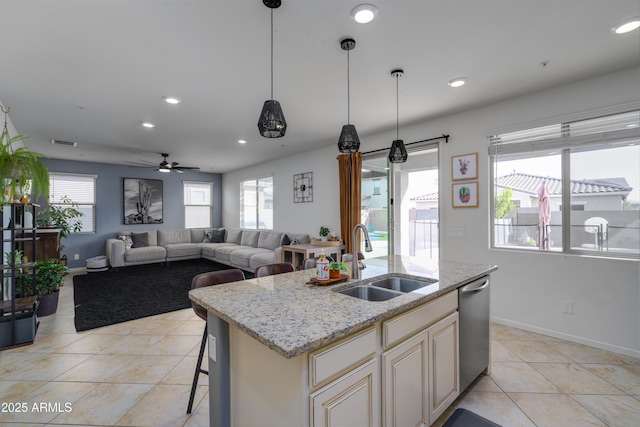 kitchen with sink, light stone counters, decorative light fixtures, stainless steel dishwasher, and a kitchen island with sink