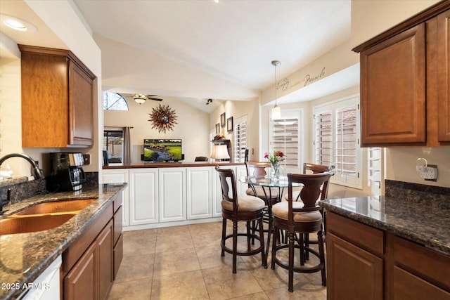 kitchen with ceiling fan, vaulted ceiling, dark stone countertops, sink, and light tile patterned floors