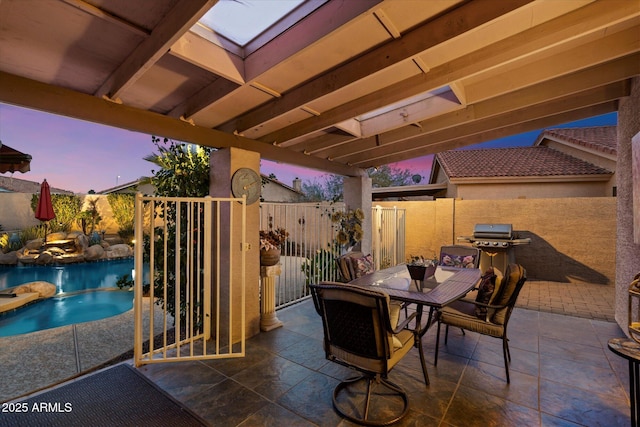 patio terrace at dusk with a fenced in pool and area for grilling