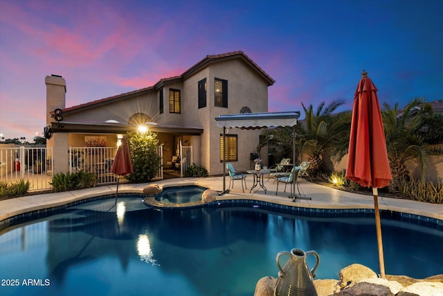 pool at dusk featuring a patio area and an in ground hot tub