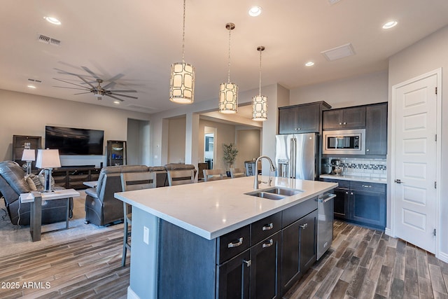 kitchen featuring sink, hanging light fixtures, appliances with stainless steel finishes, a kitchen island with sink, and decorative backsplash