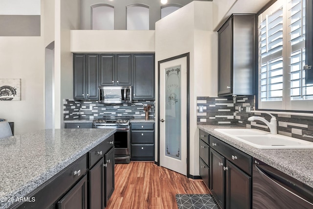 kitchen with backsplash, sink, light hardwood / wood-style flooring, stainless steel appliances, and light stone counters