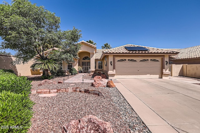 mediterranean / spanish house featuring stucco siding, a tiled roof, concrete driveway, solar panels, and an attached garage