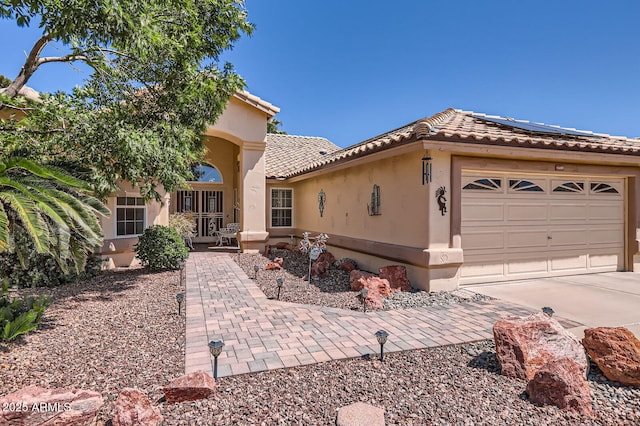 mediterranean / spanish home featuring a tile roof, concrete driveway, solar panels, and stucco siding
