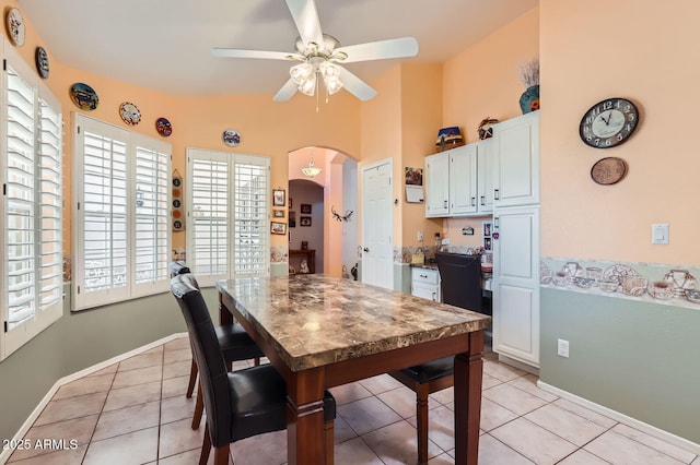 dining space with light tile patterned flooring, a ceiling fan, baseboards, and arched walkways
