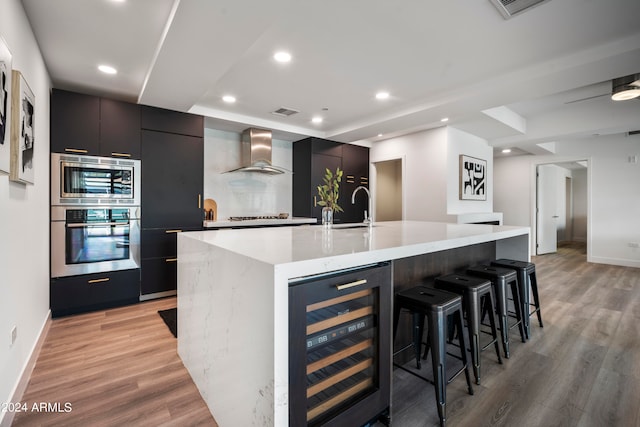 kitchen with wine cooler, sink, wall chimney exhaust hood, light hardwood / wood-style flooring, and a spacious island