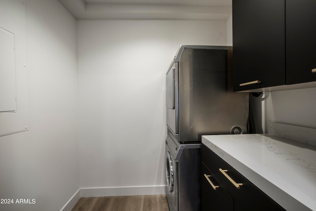 laundry room with cabinets, hardwood / wood-style floors, and stacked washer and clothes dryer