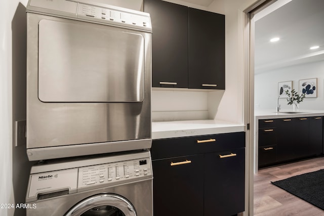 clothes washing area with light wood-type flooring, stacked washer / dryer, sink, and cabinets