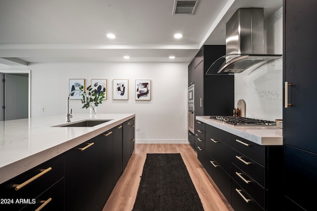 kitchen featuring light wood-type flooring, wall chimney exhaust hood, stainless steel gas cooktop, and sink