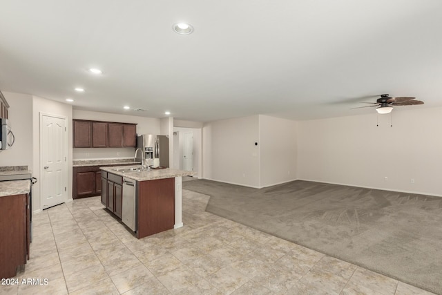 kitchen with appliances with stainless steel finishes, an island with sink, sink, dark brown cabinets, and light carpet