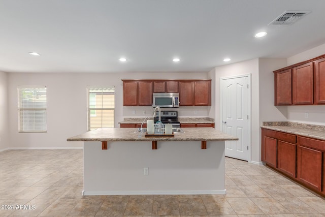 kitchen with a kitchen bar, appliances with stainless steel finishes, sink, and an island with sink