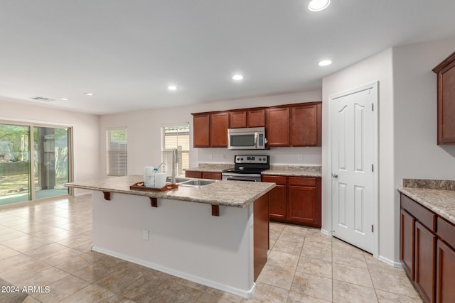 kitchen with light tile patterned flooring, appliances with stainless steel finishes, sink, a kitchen breakfast bar, and a kitchen island with sink