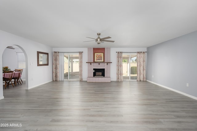 unfurnished living room featuring ceiling fan, a fireplace, baseboards, and wood finished floors