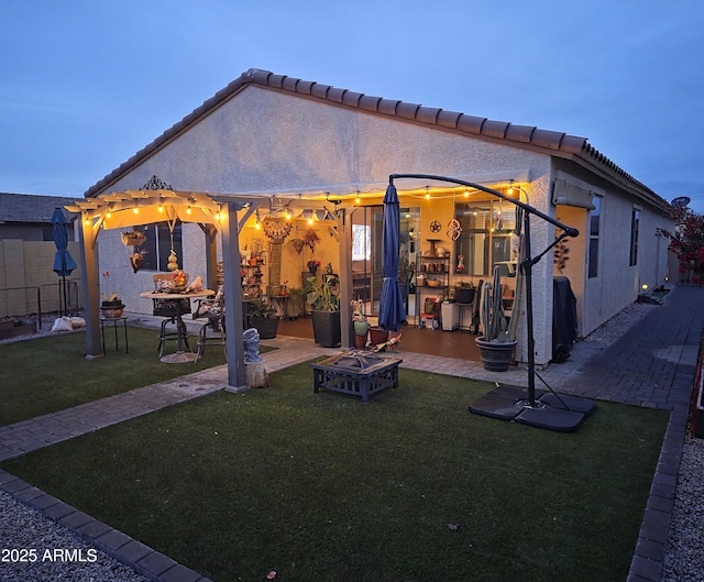 rear view of property featuring an outdoor fire pit, a lawn, a pergola, and stucco siding