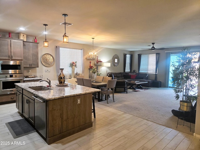 kitchen featuring a center island with sink, hanging light fixtures, appliances with stainless steel finishes, a sink, and dark brown cabinets