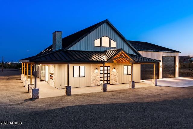 rear view of property with a chimney, a standing seam roof, metal roof, driveway, and an attached garage