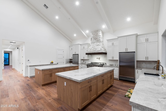 kitchen featuring a spacious island, stainless steel appliances, custom range hood, a sink, and high vaulted ceiling