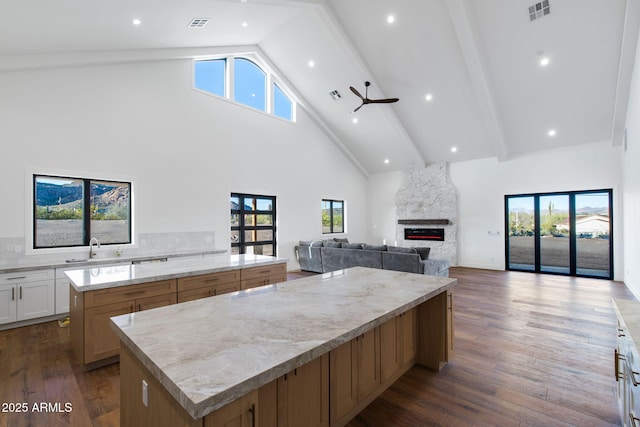kitchen with visible vents, a spacious island, a stone fireplace, a sink, and high vaulted ceiling