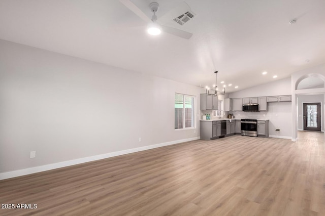 unfurnished living room featuring vaulted ceiling, ceiling fan with notable chandelier, and light wood-type flooring