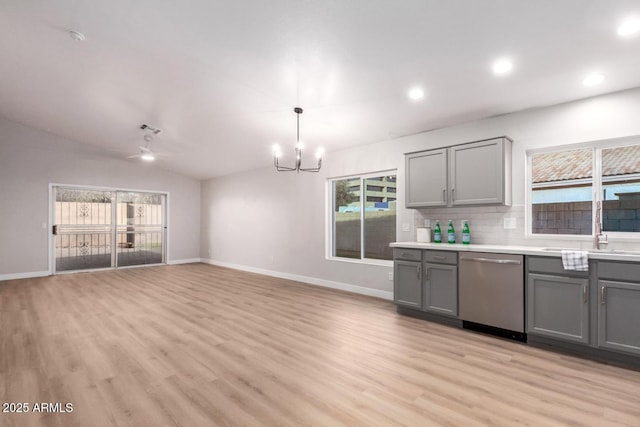 kitchen featuring gray cabinets, vaulted ceiling, decorative light fixtures, stainless steel dishwasher, and light hardwood / wood-style floors