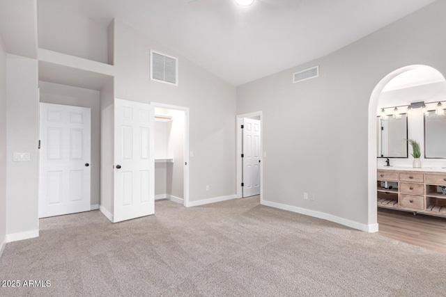 unfurnished bedroom with connected bathroom, a spacious closet, high vaulted ceiling, and light carpet