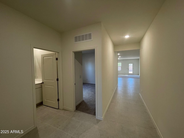 hallway with light tile patterned floors, visible vents, and baseboards