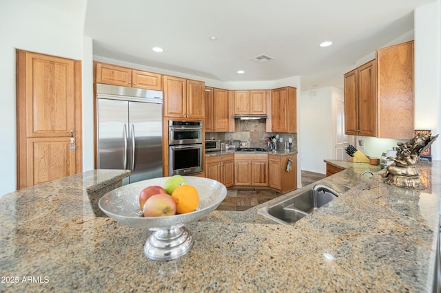 kitchen featuring sink, backsplash, light stone counters, kitchen peninsula, and stainless steel appliances