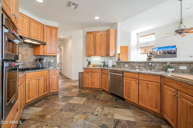 kitchen with sink, dark stone countertops, appliances with stainless steel finishes, ceiling fan, and decorative backsplash