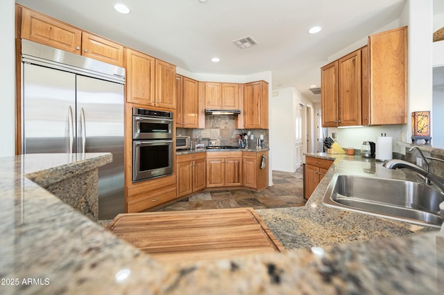 kitchen with light stone countertops, appliances with stainless steel finishes, sink, and decorative backsplash