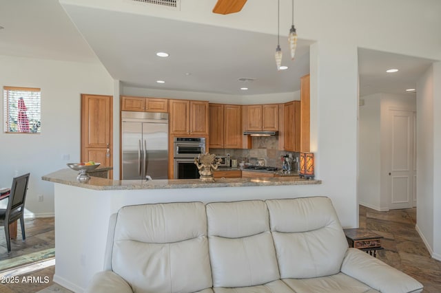 kitchen with appliances with stainless steel finishes, backsplash, light stone counters, decorative light fixtures, and kitchen peninsula