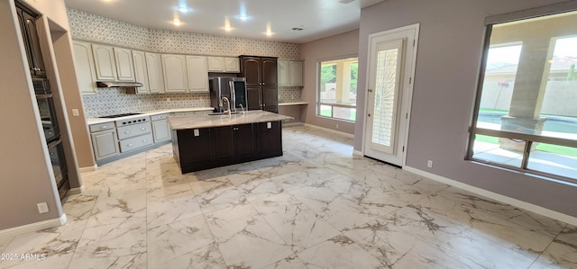 kitchen with marble finish floor, an island with sink, and baseboards